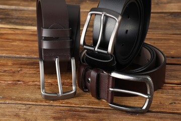 Three leather belts on wooden table, closeup
