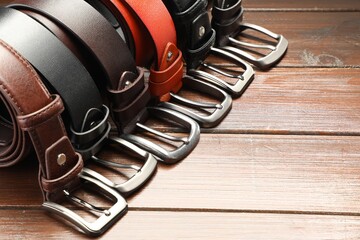 Many leather belts on wooden table, closeup. Space for text
