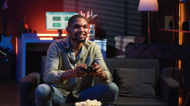 Cheerful confident person winning the video games championship, celebrating and feeling pleased with his success. Happy joyous black guy enjoying free time and a gaming win. Camera B.