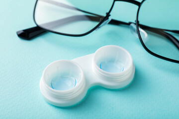 Contact lenses in case and glasses on turquoise background, closeup