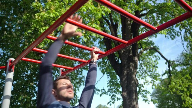 Male athlete training on red monkey bars in outdoor gym. Man doing sport exercises in open air park for wellness and body control. Concept of fitness, endurance and healthy lifestyle