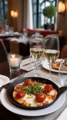Close-up of a personal pizza with tomatoes served with wine and lit candle in a restaurant setting