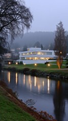 Modern white building illuminated along a foggy riverbank with reflections, landscape architecture and moody atmosphere.