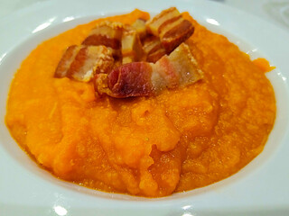 Mashed pumpkin with crispy bacon on white plate