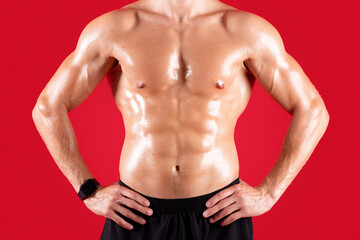 Fototapeta premium Cropped view of handsome young sportsman with bare torso posing with hands on hips over red studio background. Sexy athletic guy with prominent abs muscles, closeup view. Strength workout concept