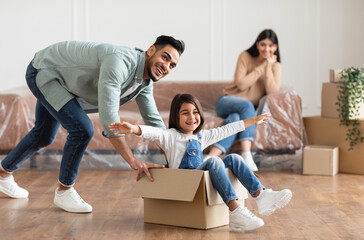 At New Apartment. Happy loving family having fun and celebrating moving day, excited man riding...