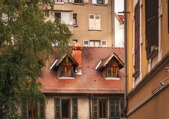 A warm, nostalgic view of old tiled roofs and wooden windows nestled between aged buildings in Annecy, France.