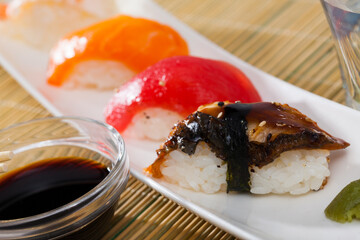 Delicious nigiri sushi set with tuna, salmon, shrimp and eel served on white plate with piquant wasabi paste and soy sauce..