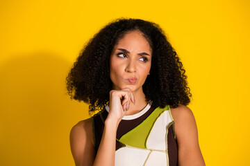 Young woman with curly hair thinking against a vibrant yellow background