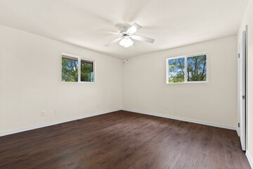 An empty room featuring a ceiling fan and two windows that illuminate the space