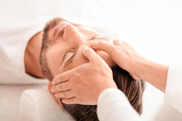 Peaceful bearded man getting healing head massage at modern luxury spa, top view. Spa therapist or...