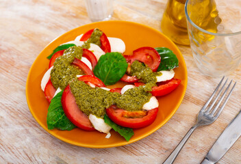 Italian salad, caprese with basil leaves and pesto sauce, served on table.