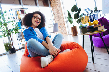 Young female professional sitting in a casual office environment on a bean bag, exhibiting...