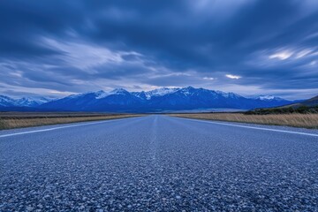 Empty asphalt road stretches into a dramatic mountain range under a stormy sky.  Vast, serene landscape