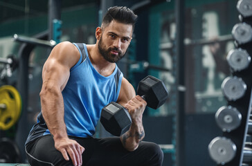 Wightlifting workout. Handsome bodybuilder picking up dumbbells at gym, empty space