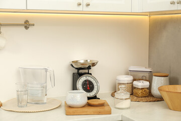 Retro mechanical kitchen scale, different utensils and food products on white marble countertop indoors