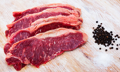 Obraz premium Pieces of raw boneless marbled beef on wooden background with seasonings prepared for roasting