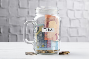 Tips jar with money on white marble table