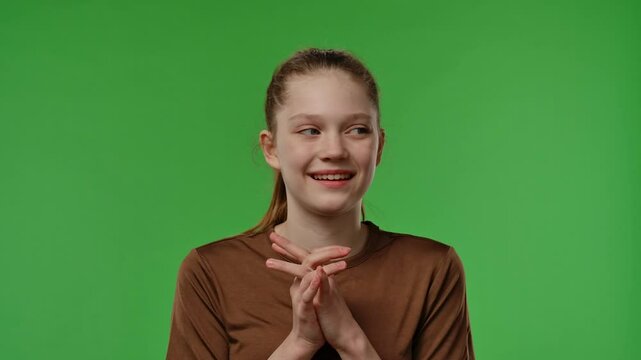 Teenage girl posing in front of camera with folded palms, pitiful facial expression, isolated on chromakey green screen studio background.