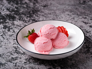 Three scoops of pink strawberry ice cream, served with fresh strawberries on a white plate