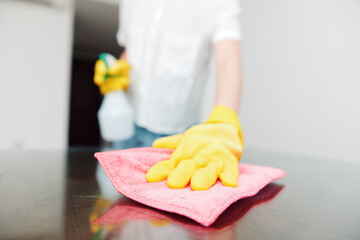 Cleaning woman in yellow rubber gloves wiping table with cleaning solution bottle on top
