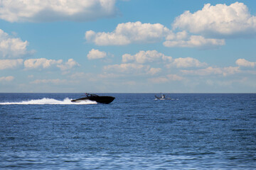 black ocean speedboat passing old fishing boat with sky and clouds