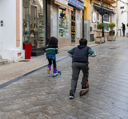two kids riding scooters on old stone street