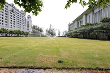 Closeup of Sprinkler Splash Water over grass field to water in the grass among the buildings at Thailand.