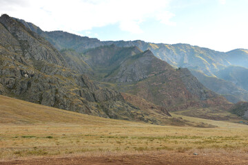 The edge of a wide, dry steppe at the foot of a high mountain range on a cloudy day in early autumn.