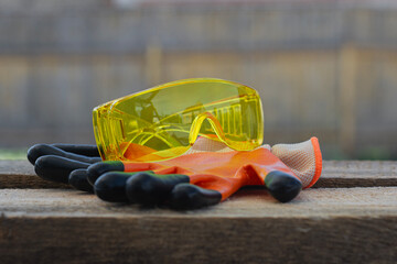 Yellow safety goggles and orange gloves rest on a rustic wooden surface. Concept workplace safety...