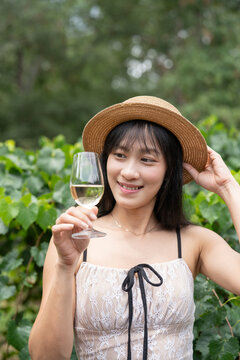 Elegant Asian Woman Savoring White Wine at a Scenic Winery.