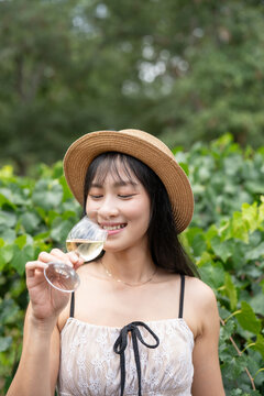 Elegant Asian Woman Savoring White Wine at a Scenic Winery.