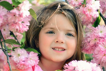 Spring child girl under blooming sakura. Dreamy girl in flower garden. Portrait of happy teen girl in spring. Little child face close-up. Dreamy kids face among spring flowers. Spring girls face.