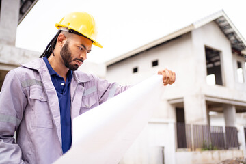 Hispanic male engineer holding blueprints at a construction site, reviewing housing project progress.