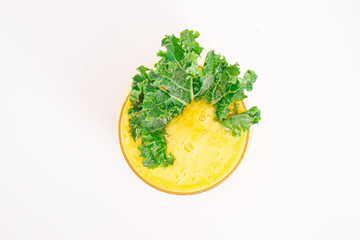 yellow fruit smoothie or juice served in clear glass and garnished with fresh curly kale on clean white background. High quality photo