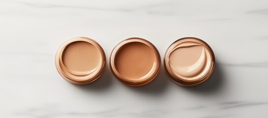 Three jars of light beige cream cosmetic products, likely foundation or moisturizer, sit on a white marble surface