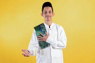 Smiling muslim man wear white shirts with Islamic ornaments and a prayer mat on the shoulder with welcoming or showing gesture
