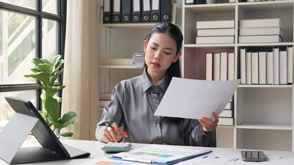 Professional female accountant carefully analyzing financial documents, using calculator and tablet in modern, well organized office workspace with natural light and corporate setting