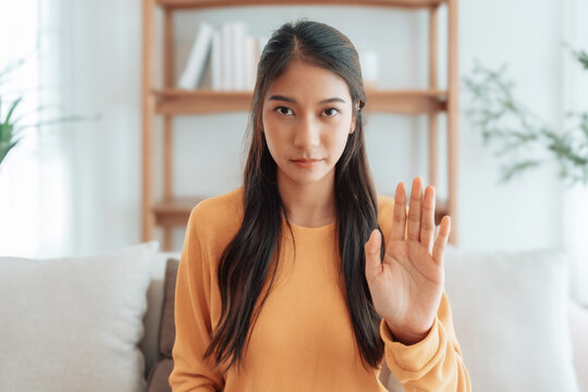 Young Asian woman with serious expression raising her hand stop gesture. Concept of protest against harassment, discrimination, and violation of human rights. Symbol of resistance and social justice