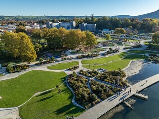 Aerial view of Rotorua Lakefront Reserve, New Zealand. People are walking and enjoying the park's playground, boardwalk, and green spaces on a sunny day.