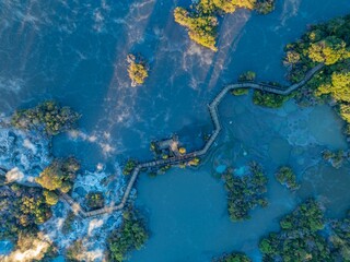 Aerial view of a wooden boardwalk winding through the geothermal landscape of Wai-O-Tapu in New Zealand. Tourists explore the unique volcanic terrain and hot springs.