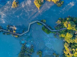 Aerial view of a wooden boardwalk winding through the geothermal landscape of Wai-O-Tapu in New Zealand. Tourists explore the unique volcanic terrain and hot springs.