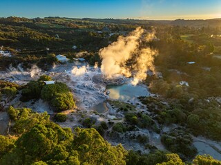 Aerial view of the Wai-O-Tapu geothermal area in Rotorua, New Zealand. Steam rises from the hot springs, a popular tourist destination due to its unique volcanic landscape.