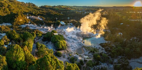 Aerial view of the Wai-O-Tapu geothermal area in Rotorua, New Zealand. Steam rises from the hot springs and geysers, showcasing the volcanic activity and unique landscape.