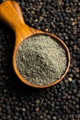 Black pepper powder in wooden cup spoon with black peppercorns background. Food ingredients. Aromatic spice. Top view