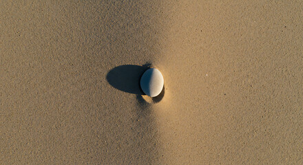 Obraz premium Serene beach stone sunlight casts shadow peaceful scene sandy texture minimalist beauty