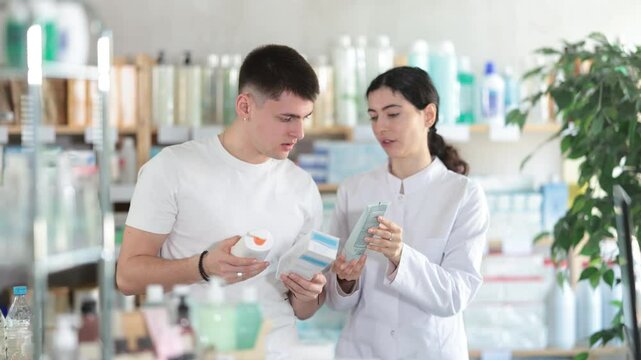 Man chooses skin cream in modern pharmacy. Female pharmacist helps with choosing a medicine. High quality 4k footage