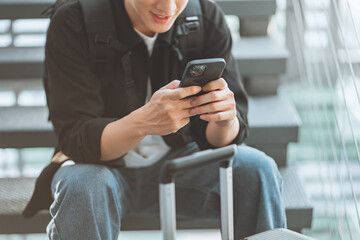 Close-up hand of smiling asian man using mobile phone at airport terminal with luggage – travel...