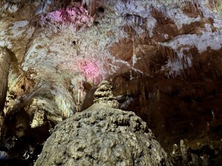 Inside a captivating cave, visitors admire fascinating rock formations illuminated by colorful lights. The vibrant hues enhance the natural beauty of the rugged surfaces and textures above