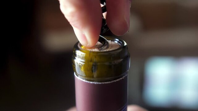 close-up shot of a corkscrew being inserted into a wine bottle's cork, capturing the moment of opening with hands holding the bottle steady.